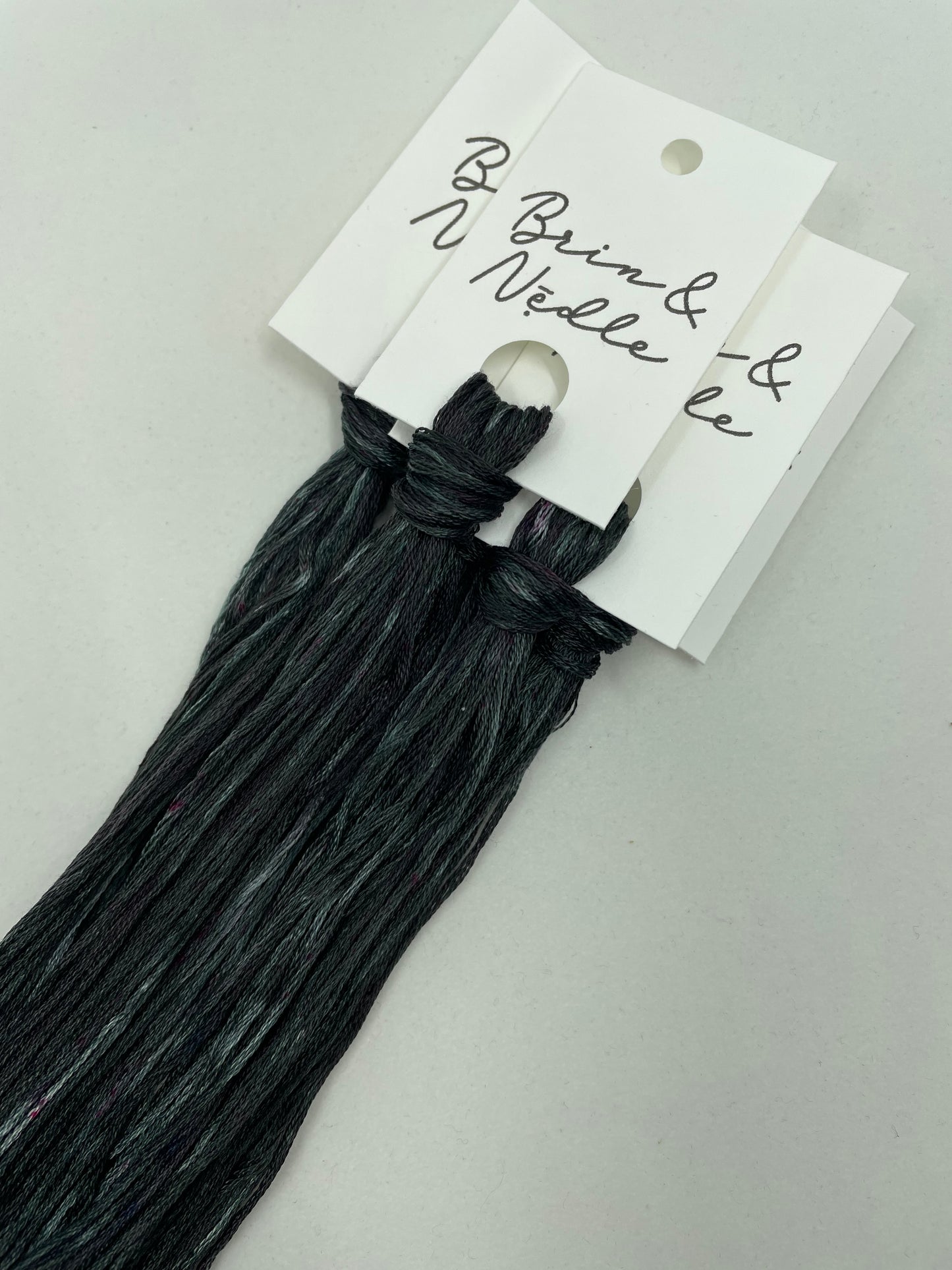 Six strand cotton floss of variegated charcoal with small hits of pink and plum
